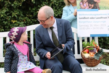 Die kleine Lia (2) sitzt mit Landrat Manfred Müller auf einer Gartenbank