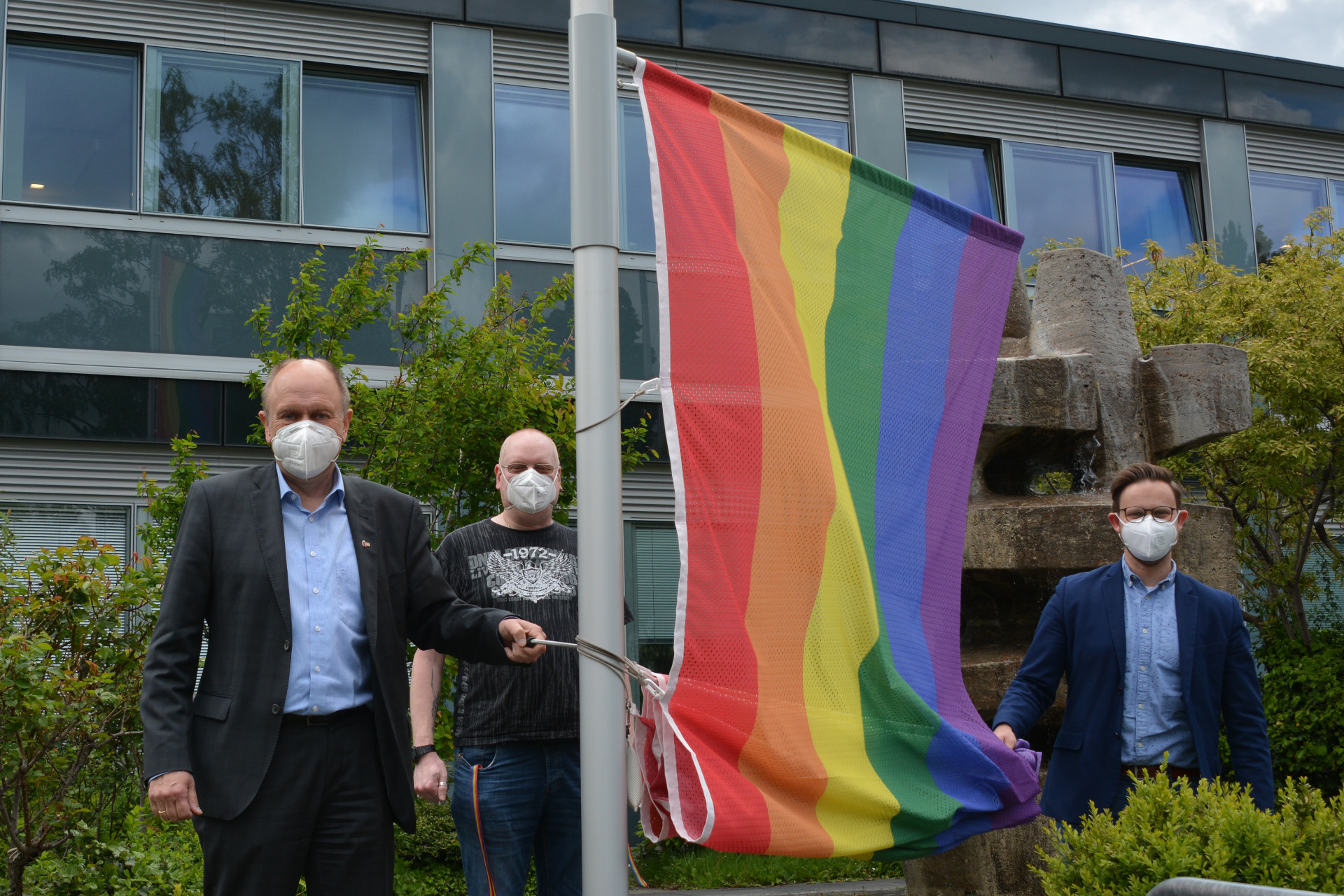 Landrat Christoph Rüther, Ecki Steinhoff (paderpride) und Dr. Sebastian Piecha (Zentrale Dienste Kreis Paderborn) hissen die Regenbogenfahne vor dem Kreishause.  Foto: Kreis Paderborn, Amt für Presse- und Öffentlichkeitsarbeit, Meike Delang
