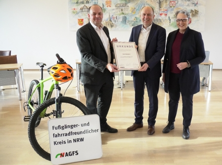 Staatssekretär Victor Haase (Ministerium für Umwelt, Naturschutz und Verkehr des Landes Nordrhein-Westfalen,l.) überreicht gemeinsam mit Christine Fuchs (AGFS-Vorstand, r.) die Urkunde an Landrat Christoph Rüther (Mitte). © Julian Sprenger, Kreis Paderborn