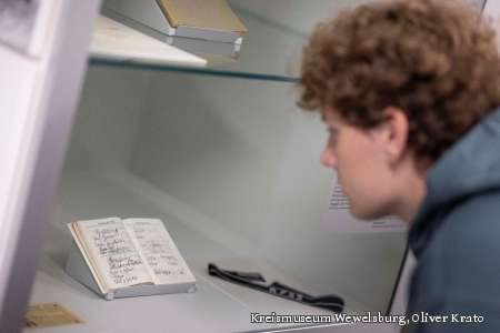 Das Bild zeigt in der Nahaufnahme einen jungen Mann, der in einer Vitrine den Taschenkalender von Heinrich Himmler anschaut